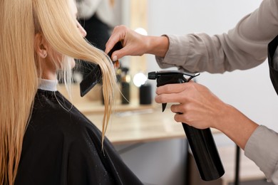 Photo of Hairdresser using spray while making stylish haircut in salon, closeup