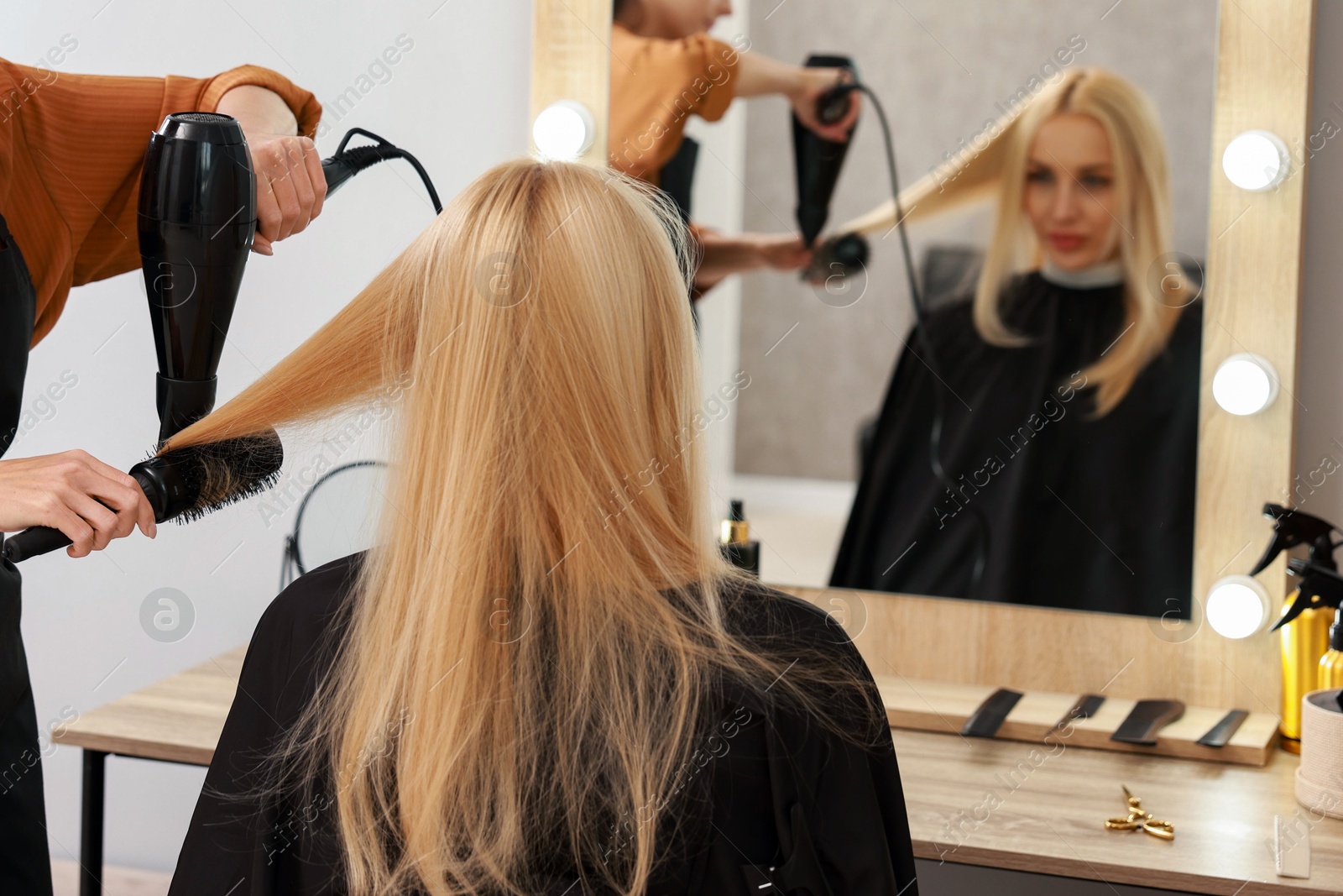 Photo of Hairdresser blow drying client's hair in salon, closeup