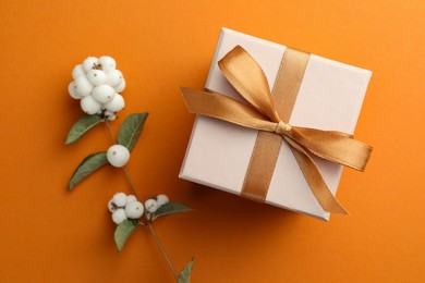 Photo of Beautiful gift box with golden bow and cotton flowers on orange background, top view