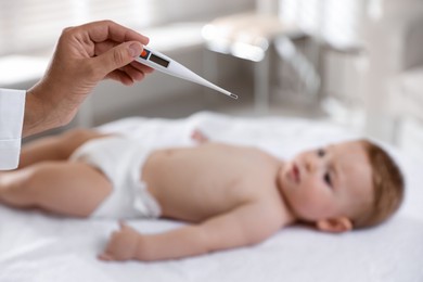 Photo of Pediatrician examining little child with thermometer in clinic, selective focus. Checking baby's health