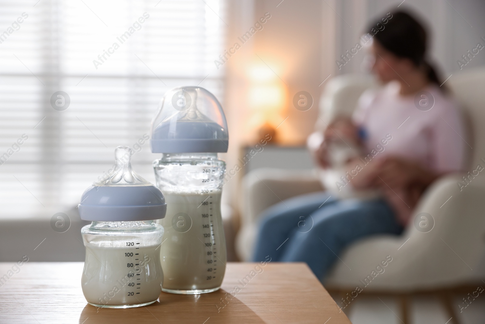 Photo of Mother holding her little baby indoors, focus on bottles with milk