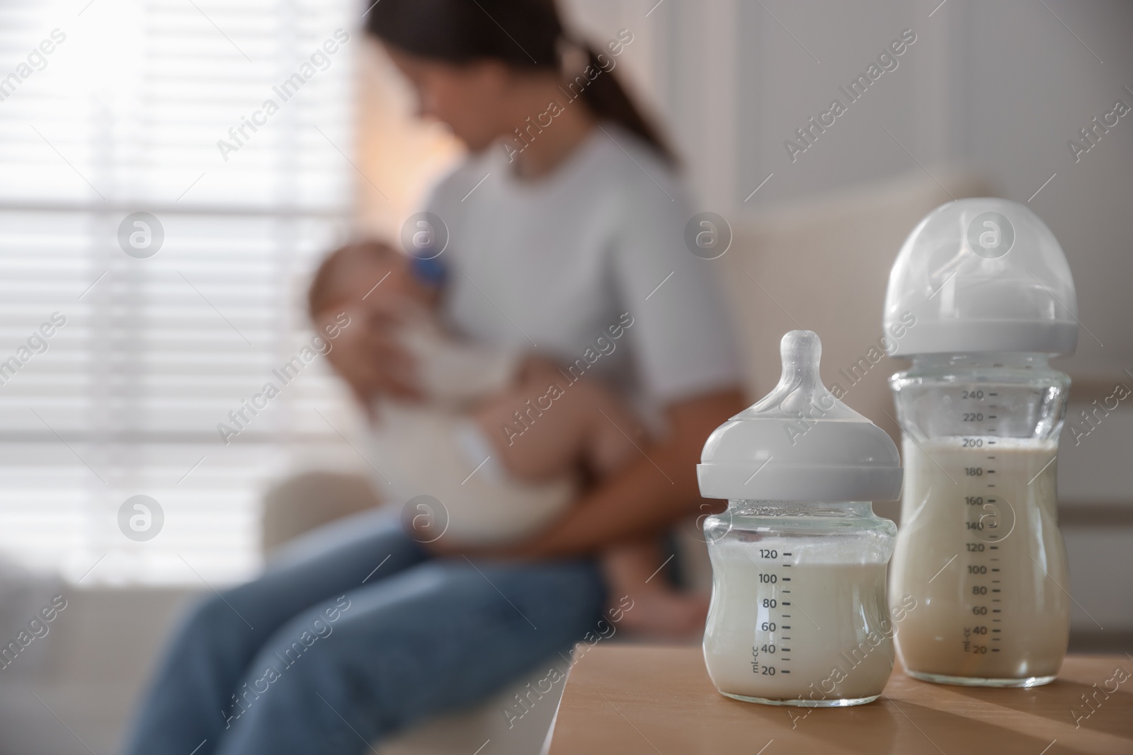 Photo of Mother holding her little baby indoors, focus on bottles with milk