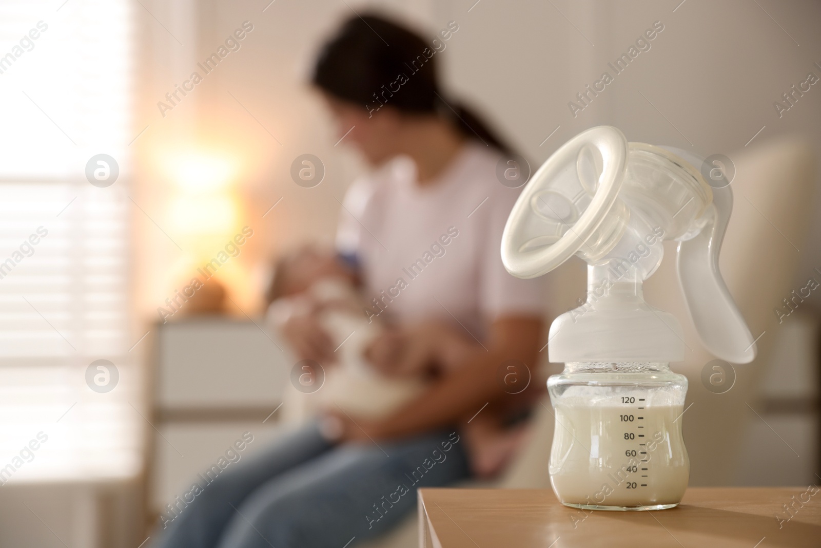 Photo of Mother holding her little baby indoors, focus on breast pump with milk