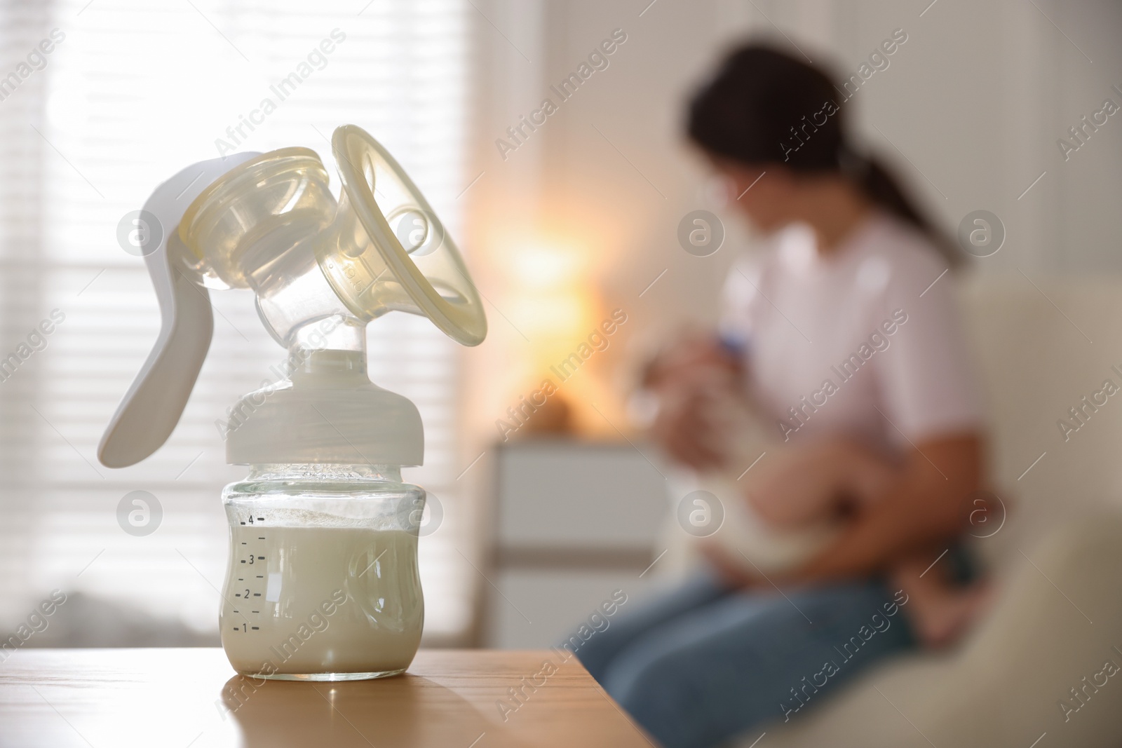 Photo of Mother holding her little baby indoors, focus on breast pump with milk