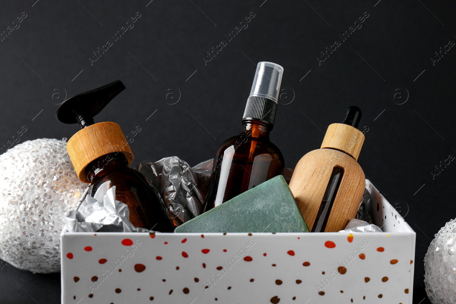 Photo of Cosmetic products in box as Christmas gift and festive balls on black background, closeup