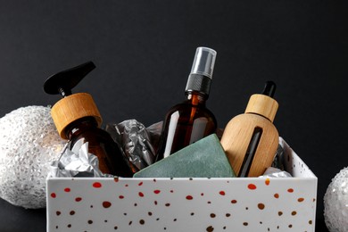 Photo of Cosmetic products in box as Christmas gift and festive balls on black background, closeup