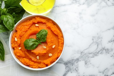 Photo of Tasty mashed sweet potato with basil and seeds in bowl on white marble table, flat lay. Space for text