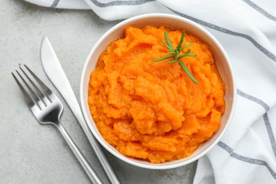 Photo of Tasty mashed sweet potato with rosemary in bowl served on grey textured table, flat lay