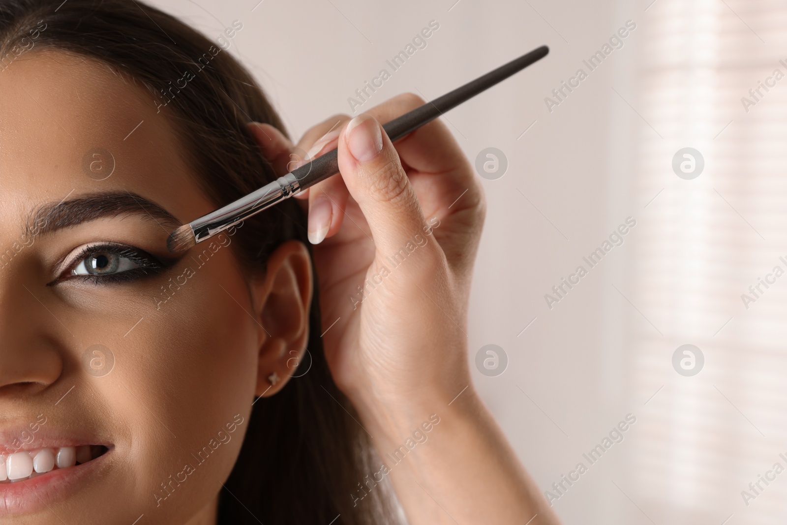 Photo of Artist doing makeup on woman's face indoors, closeup