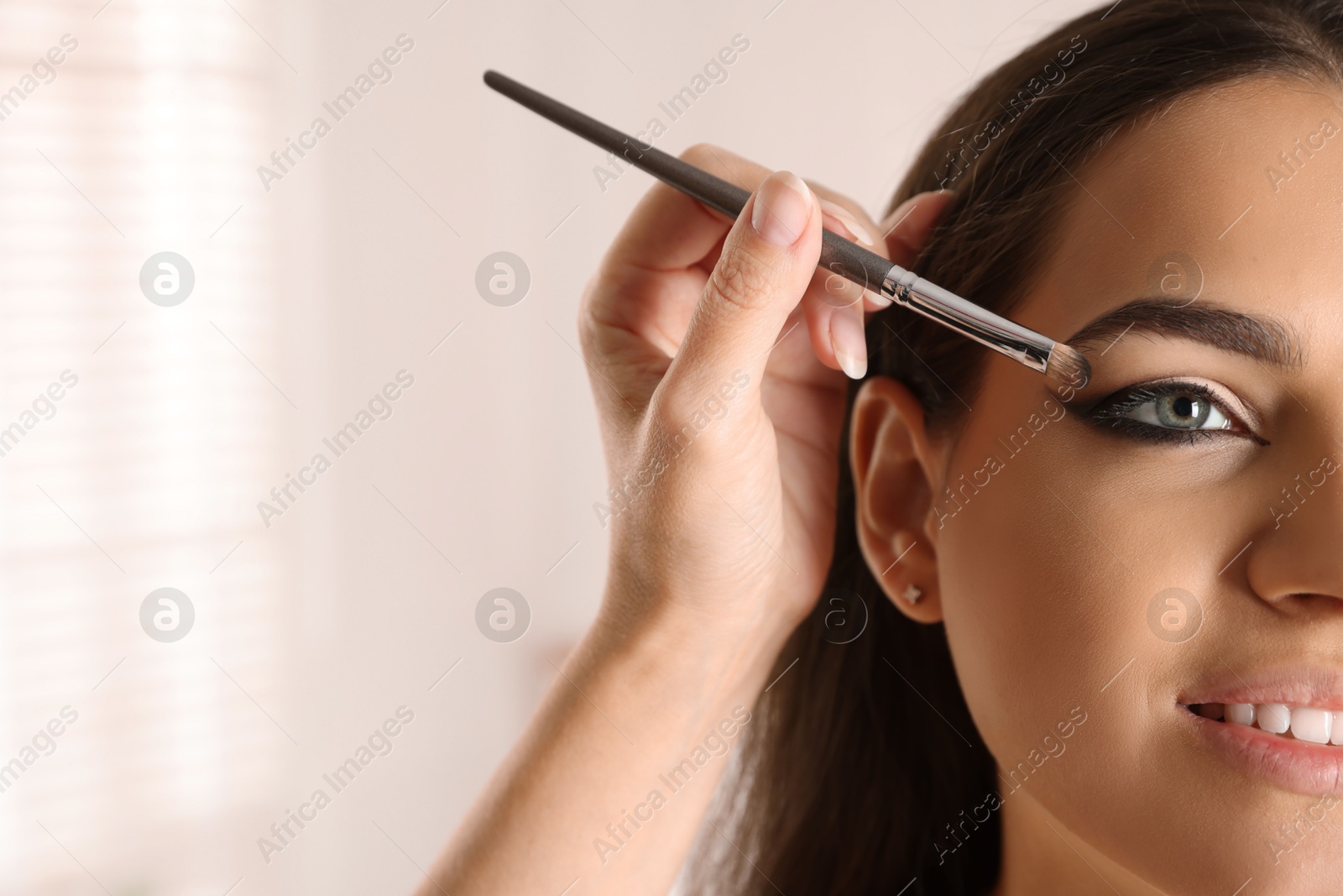 Photo of Artist doing makeup on woman's face indoors, closeup