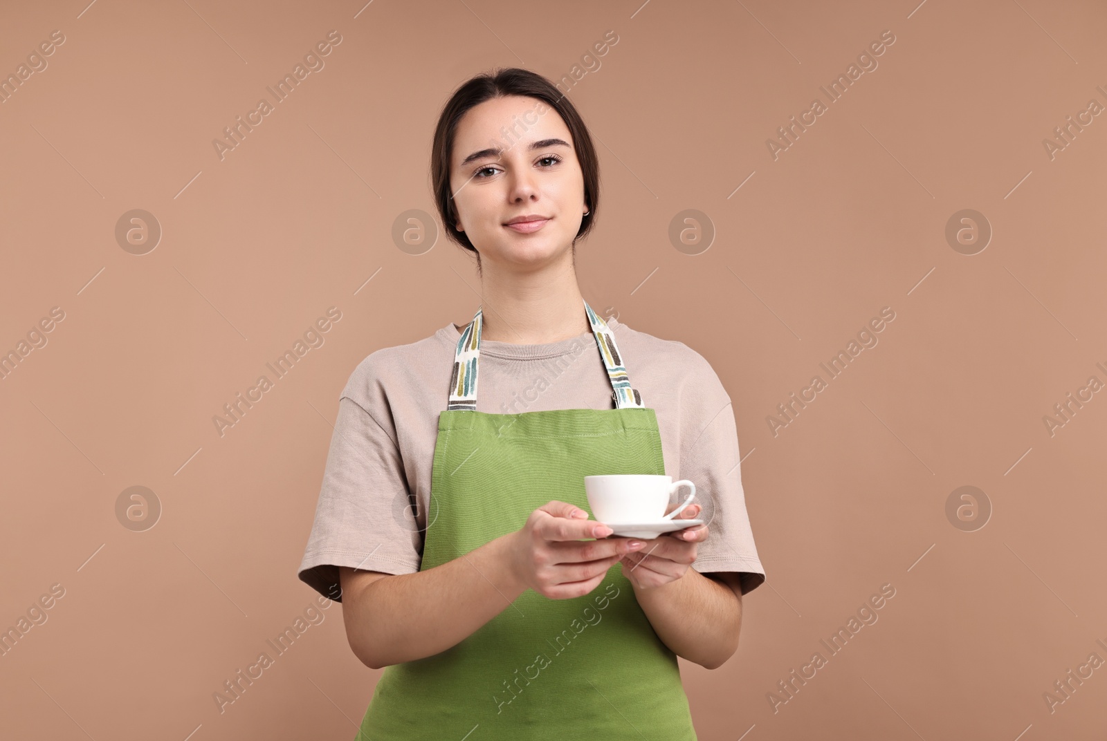 Photo of Girl in apron with cup of coffee on pale brown background. Work for teenagers