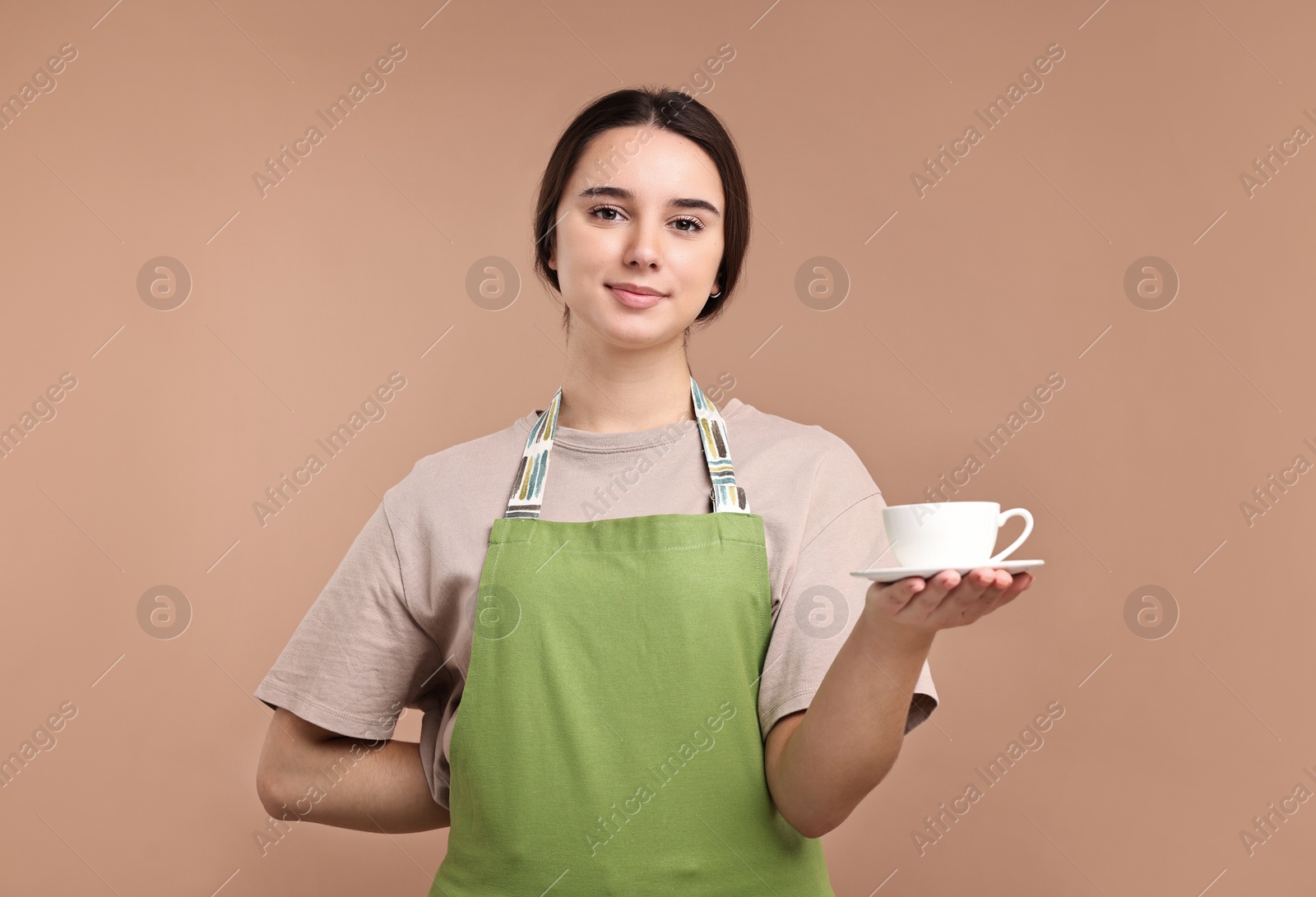 Photo of Girl in apron with cup of coffee on pale brown background. Work for teenagers