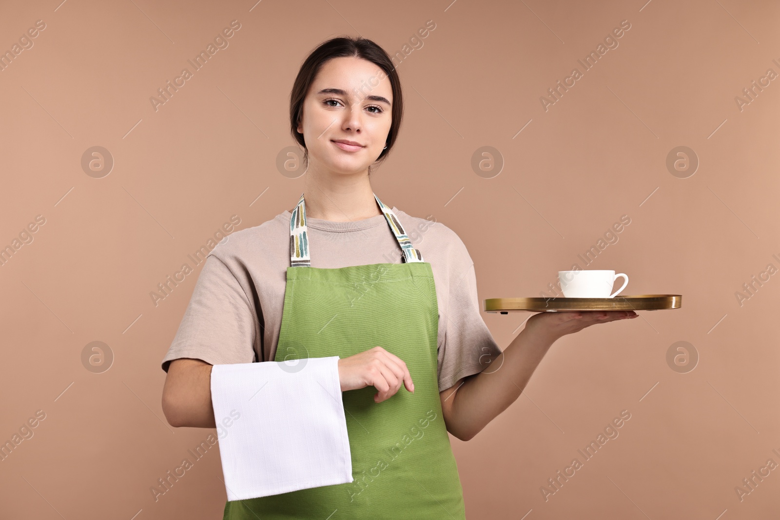 Photo of Girl in apron with cup of coffee on pale brown background. Work for teenagers