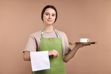 Photo of Girl in apron with cup of coffee on pale brown background. Work for teenagers