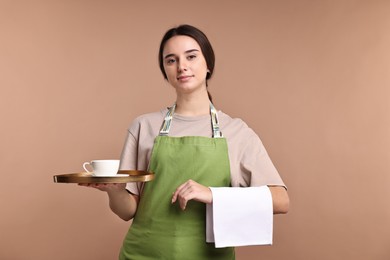 Photo of Girl in apron with cup of coffee on pale brown background. Work for teenagers