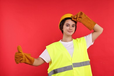 Photo of Girl with safety equipment showing thumbs up on red background. Work for teenagers