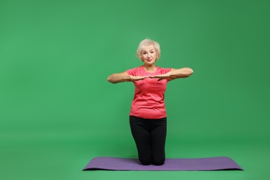 Photo of Senior woman exercising with fitness mat on green background