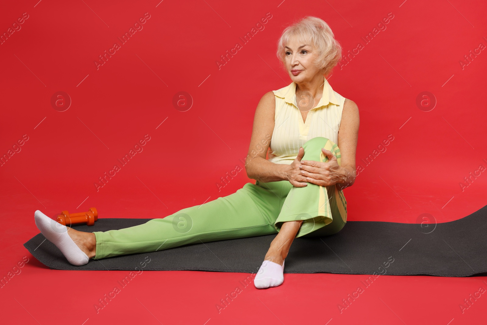 Photo of Senior woman exercising with fitness mat on red background