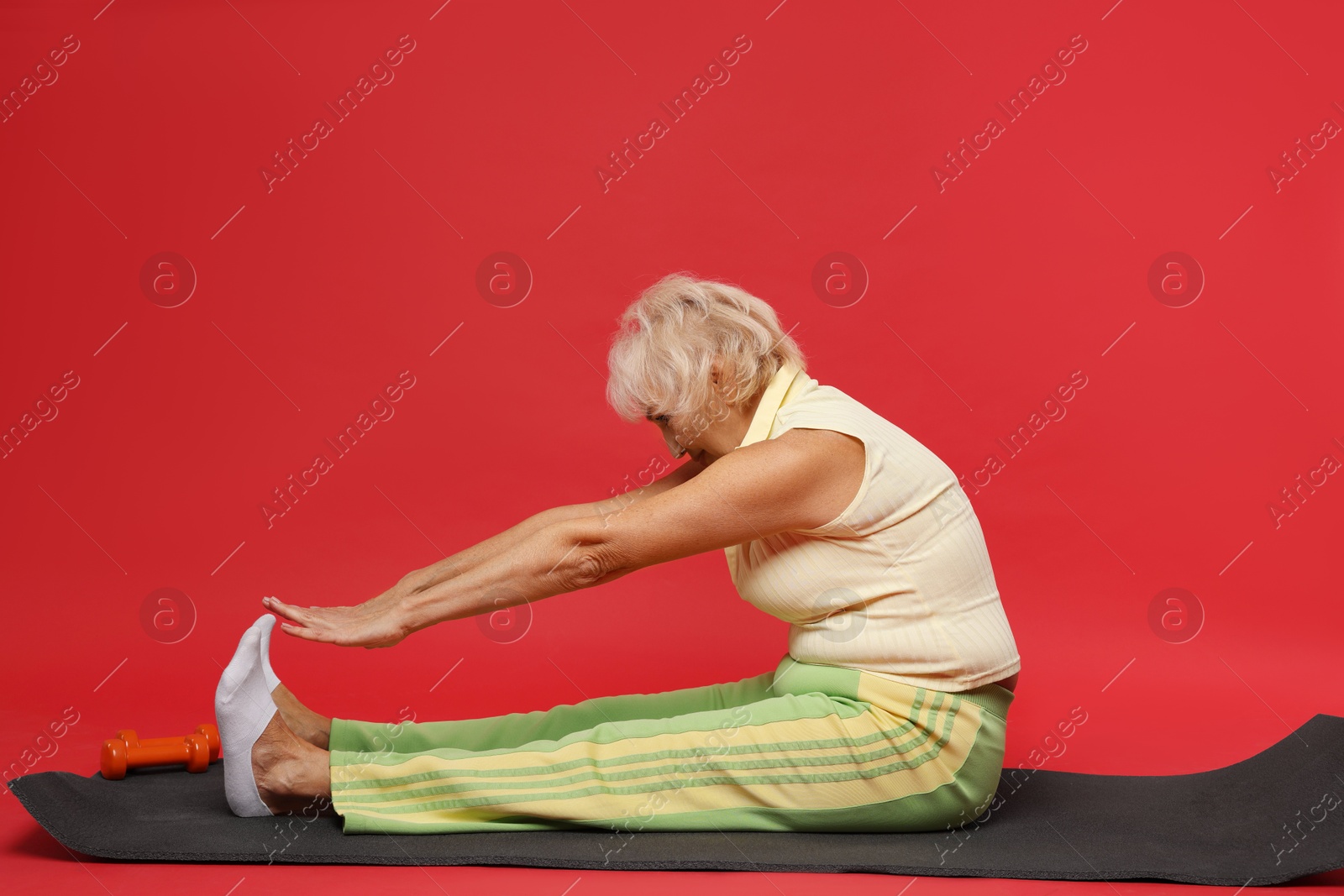 Photo of Senior woman exercising with fitness mat on red background