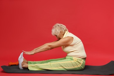 Photo of Senior woman exercising with fitness mat on red background