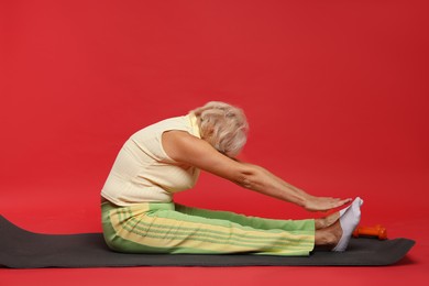 Photo of Senior woman exercising with fitness mat on red background