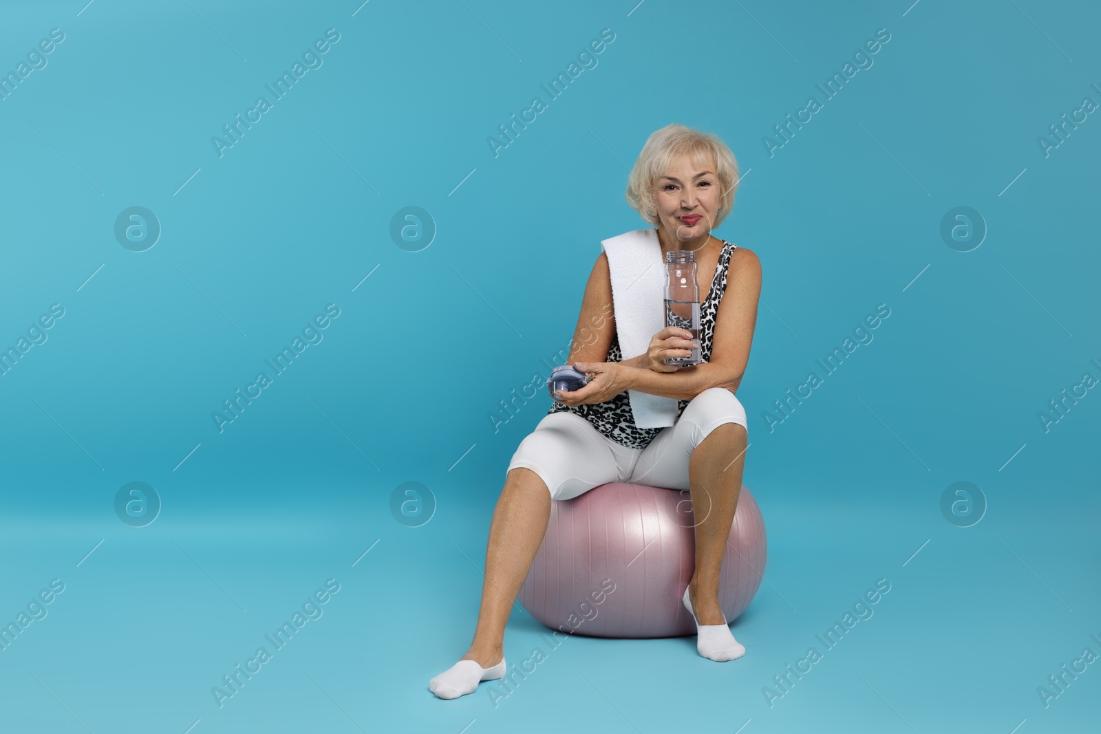 Photo of Senior woman with fitness ball, towel and water on light blue background. Space for text