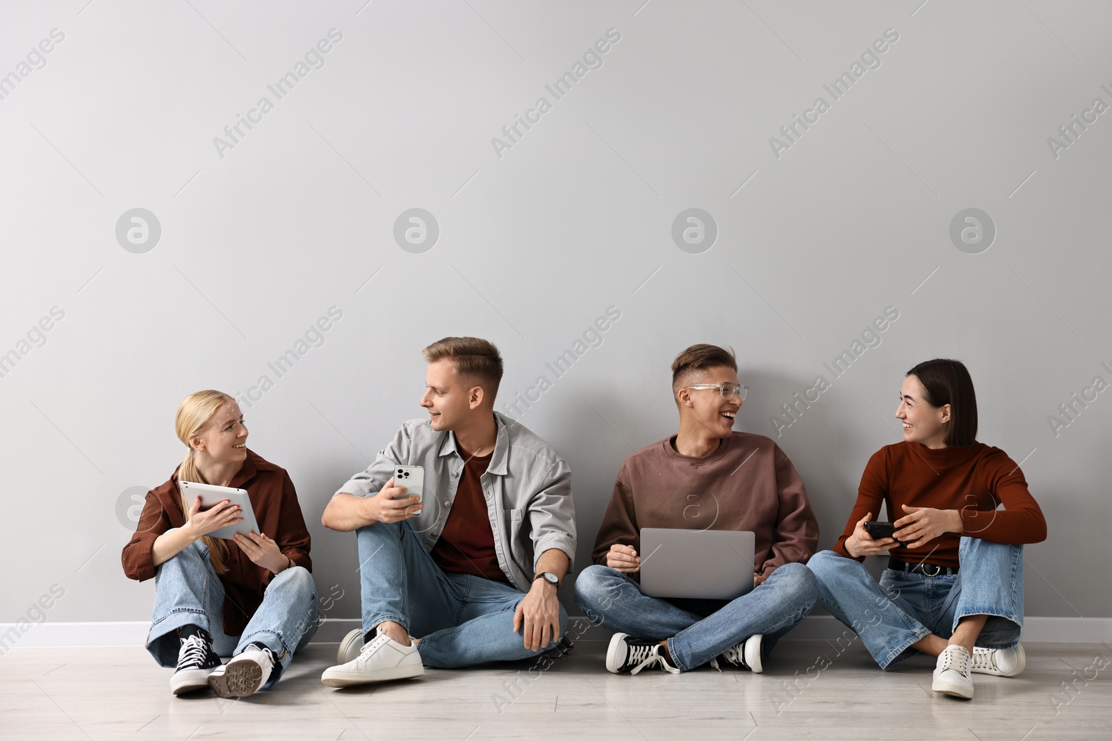 Photo of Group of people using different gadgets near light grey wall indoors. Modern technology