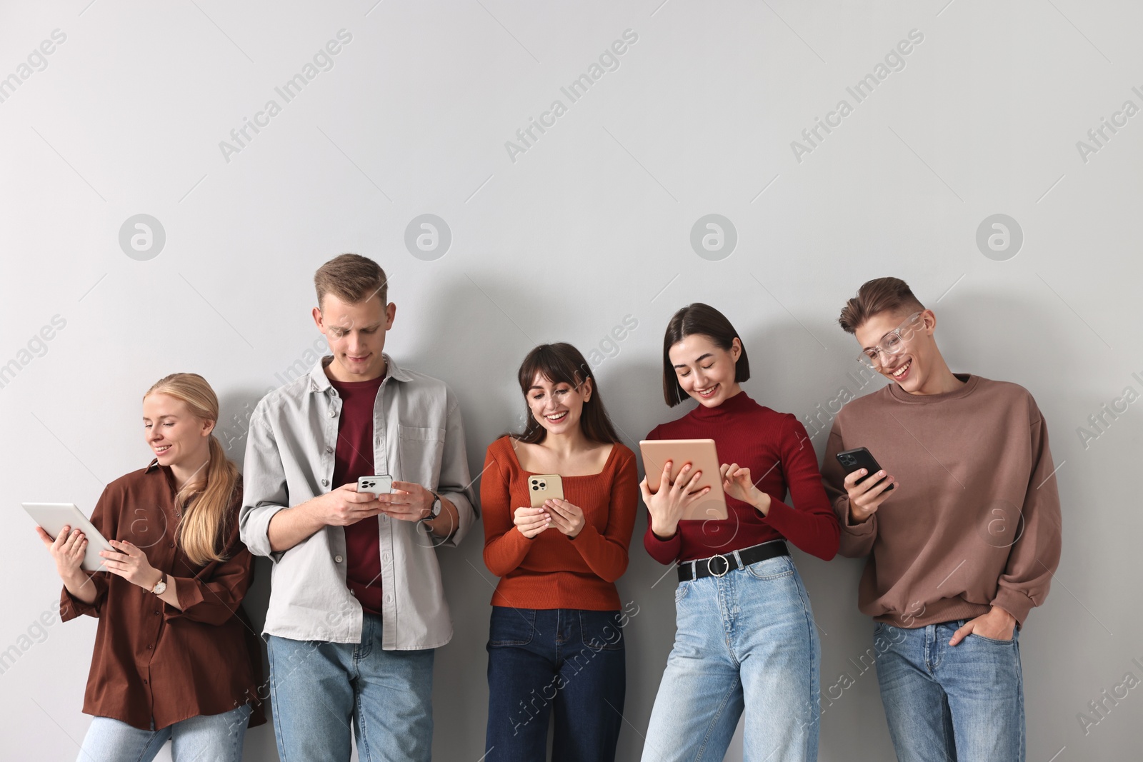 Photo of Group of people using different gadgets near light grey wall indoors. Modern technology