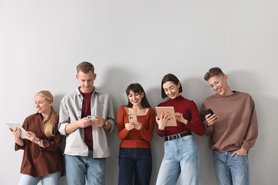 Group of people using different gadgets near light grey wall indoors. Modern technology