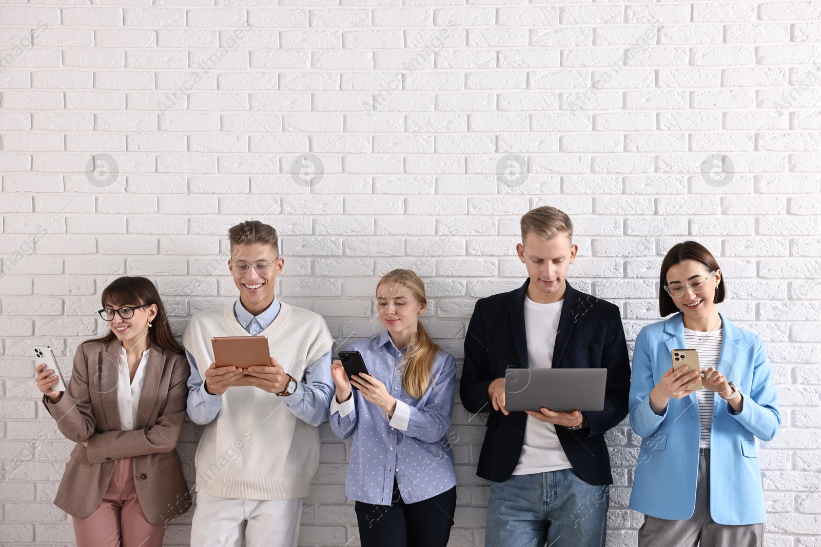 Photo of Group of people using different gadgets near white brick wall indoors. Modern technology