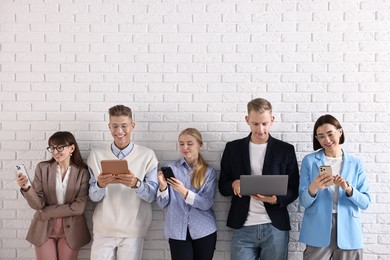 Group of people using different gadgets near white brick wall indoors. Modern technology