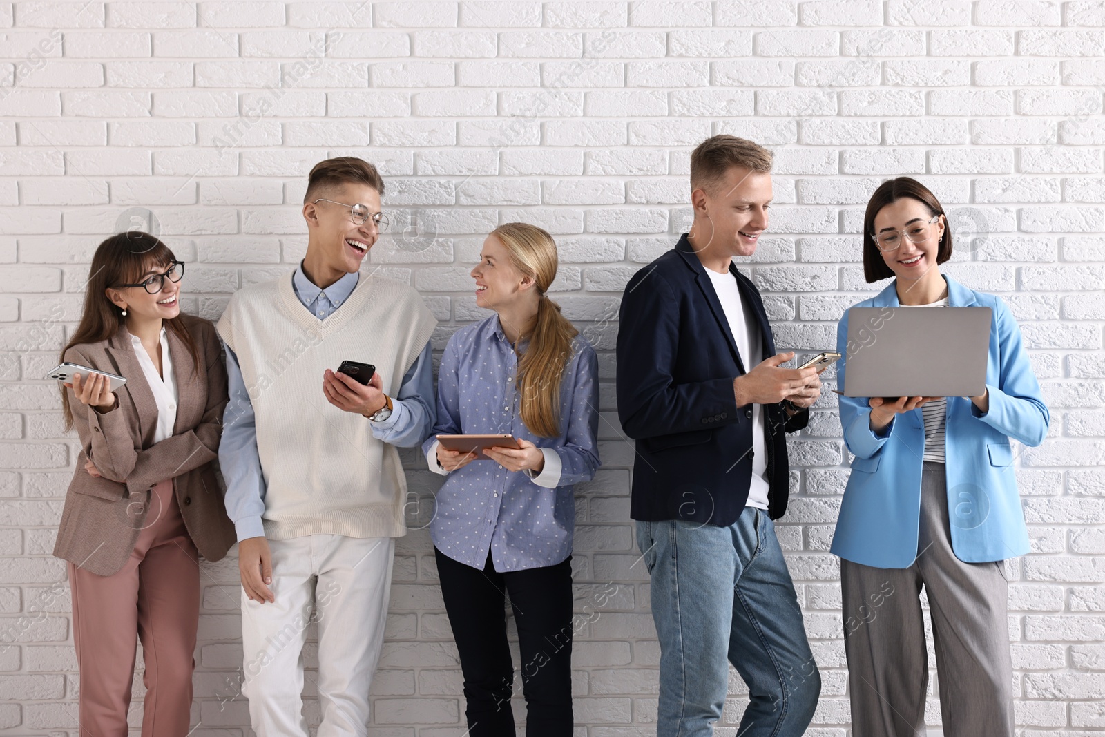 Photo of Group of people using different gadgets near white brick wall indoors. Modern technology