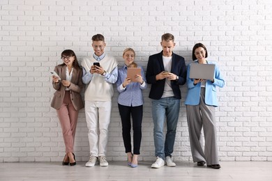 Photo of Group of people using different gadgets near white brick wall indoors. Modern technology