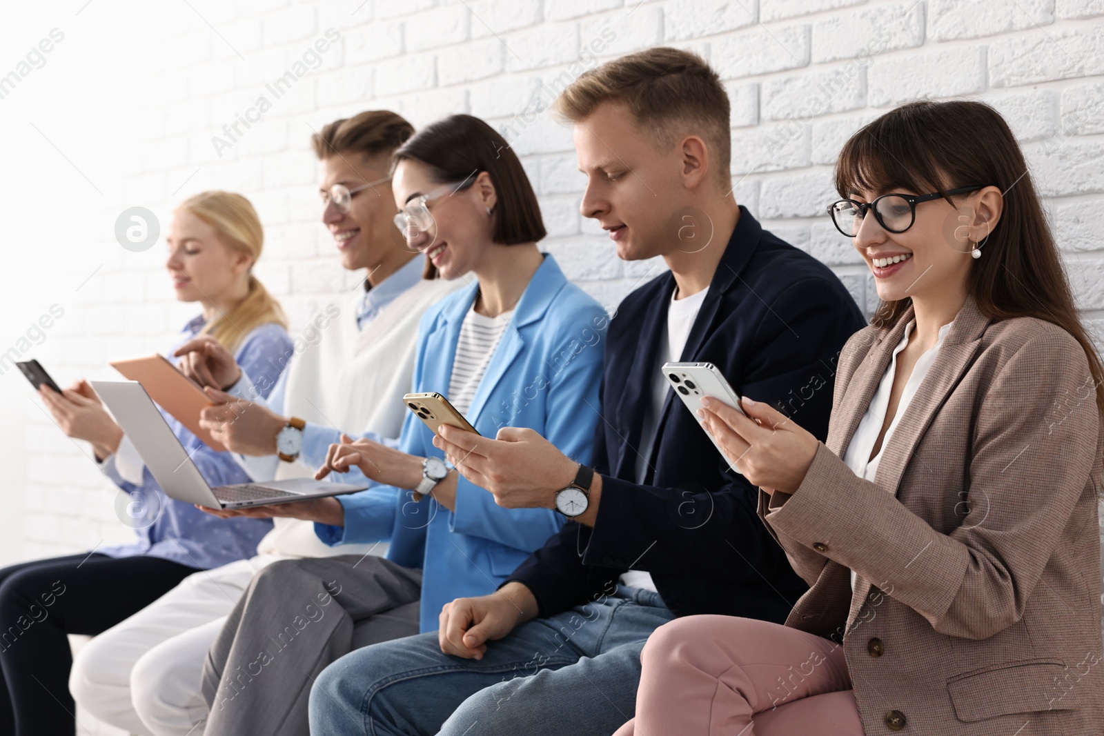 Photo of Group of people using different gadgets near white brick wall indoors. Modern technology