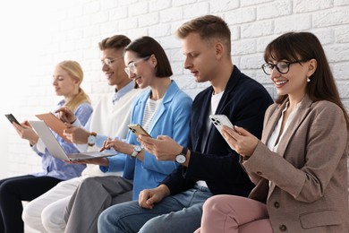 Photo of Group of people using different gadgets near white brick wall indoors. Modern technology