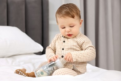 Photo of Cute little baby with money in bottle on bed at home