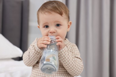 Photo of Cute little baby with money in bottle at home