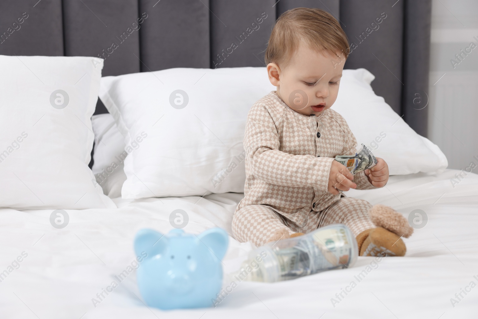 Photo of Cute little baby with money in bottle and piggybank on bed at home. Space for text