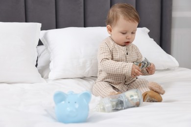 Photo of Cute little baby with money in bottle and piggybank on bed at home. Space for text