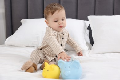 Photo of Cute little baby with piggybanks on bed at home