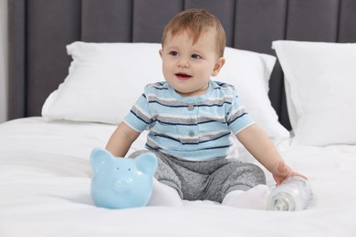 Photo of Cute little baby with money in bottle and piggybank on bed at home