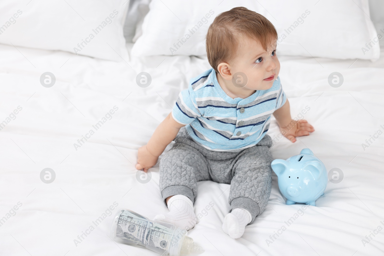 Photo of Cute little baby with money in bottle and piggybank on bed at home. Space for text