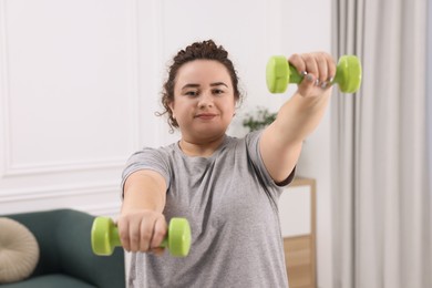 Photo of Plus size woman with dumbbells training at home