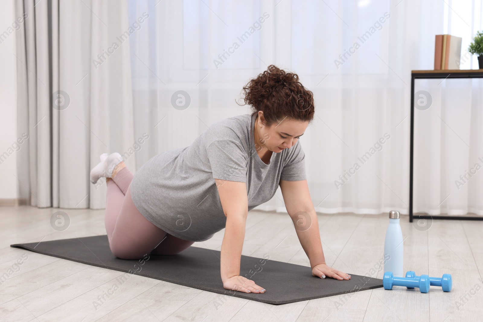 Photo of Plus size woman exercising on fitness mat at home