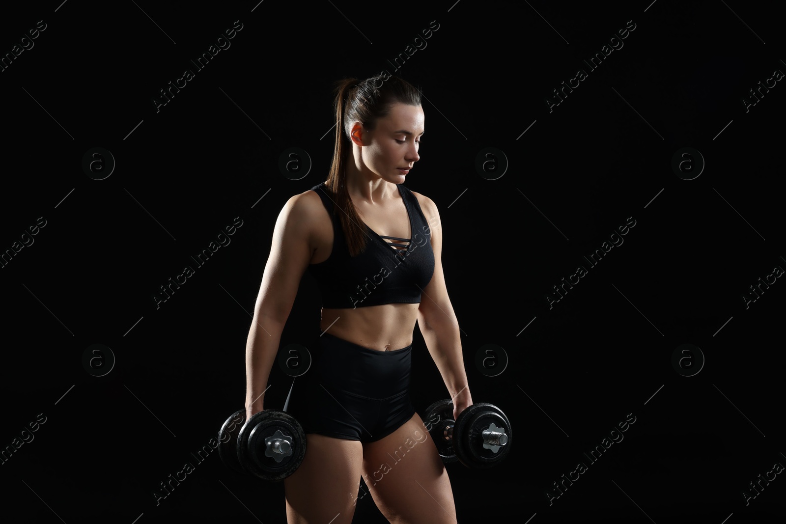 Photo of Beautiful woman in sportswear training with barbells on black background