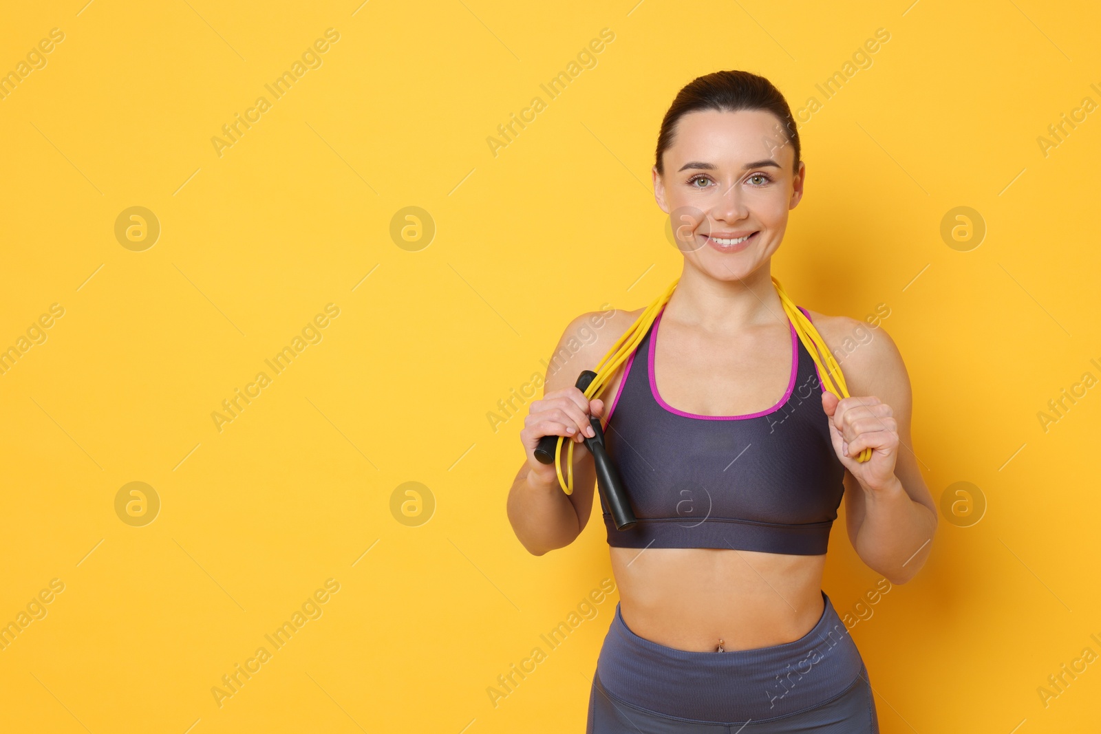 Photo of Smiling woman with skipping rope on yellow background. Space for text