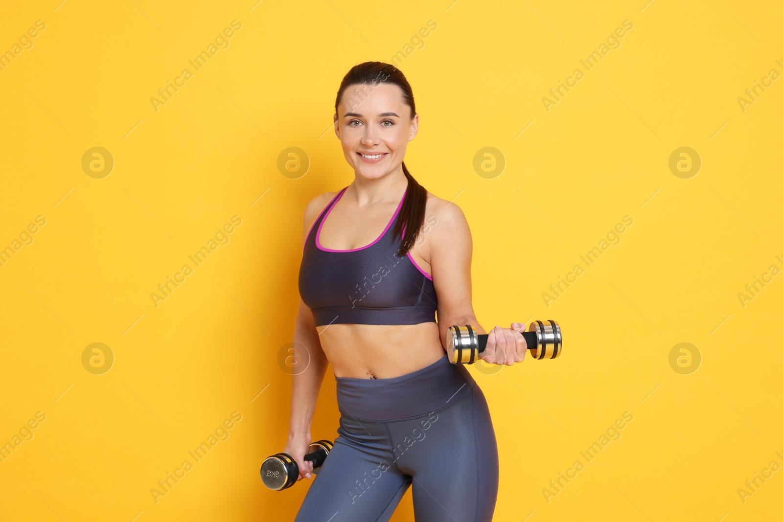 Photo of Smiling woman with dumbbells training on yellow background