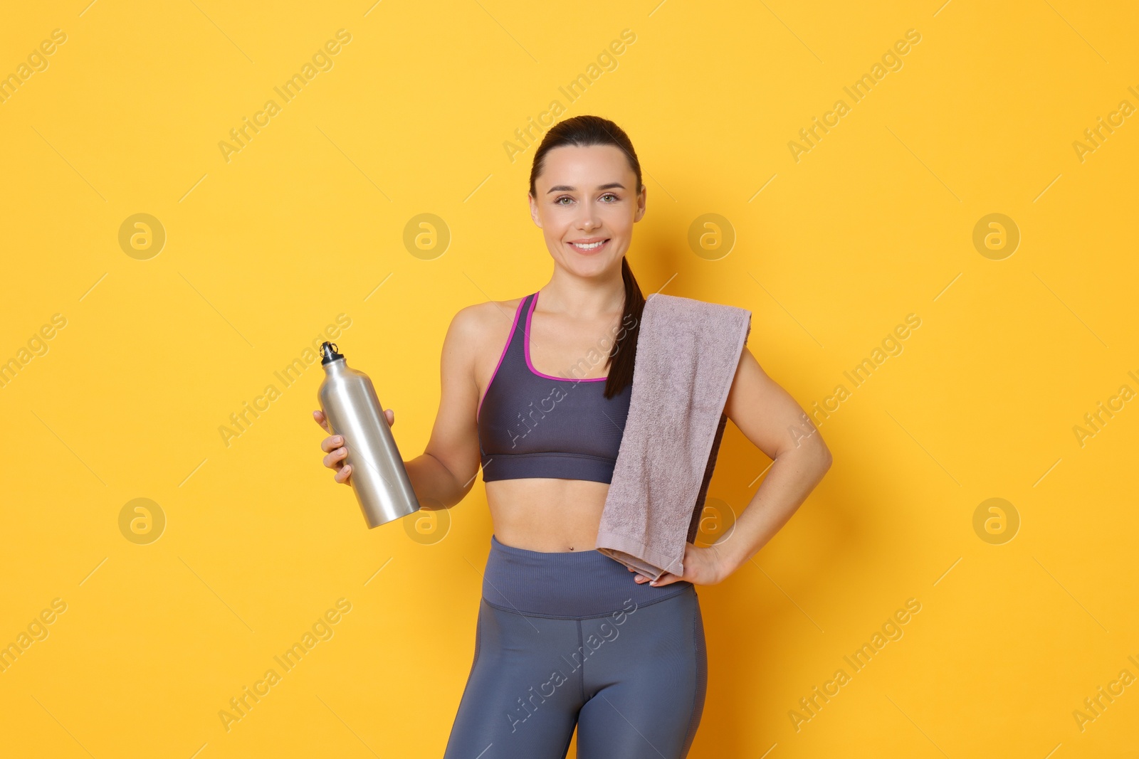 Photo of Smiling woman with thermo bottle and towel on yellow background