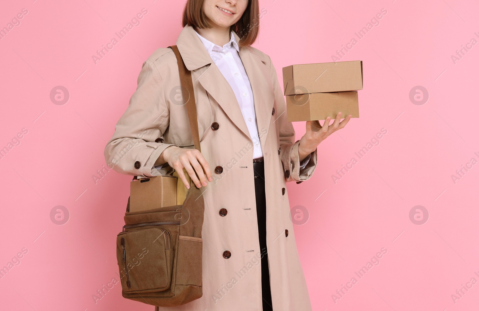 Photo of Happy postwoman with bag and parcels on pink background, closeup