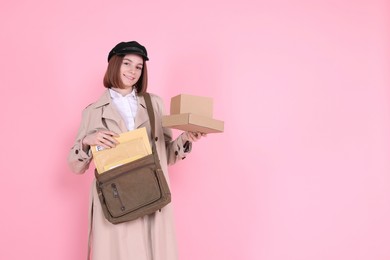 Photo of Happy postwoman with bag and parcels on pink background. Space for text